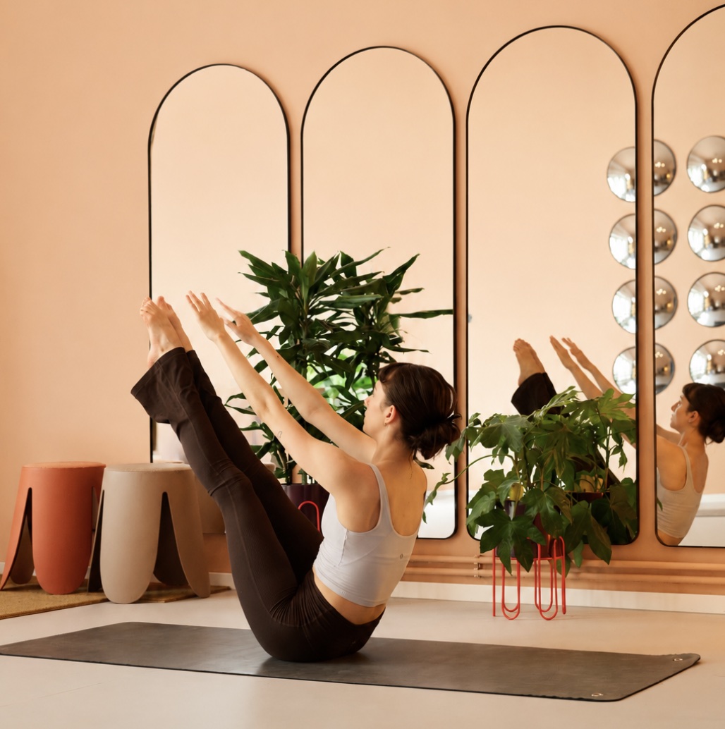 A member balancing in boat pose in front of the arched mirrors and plants
